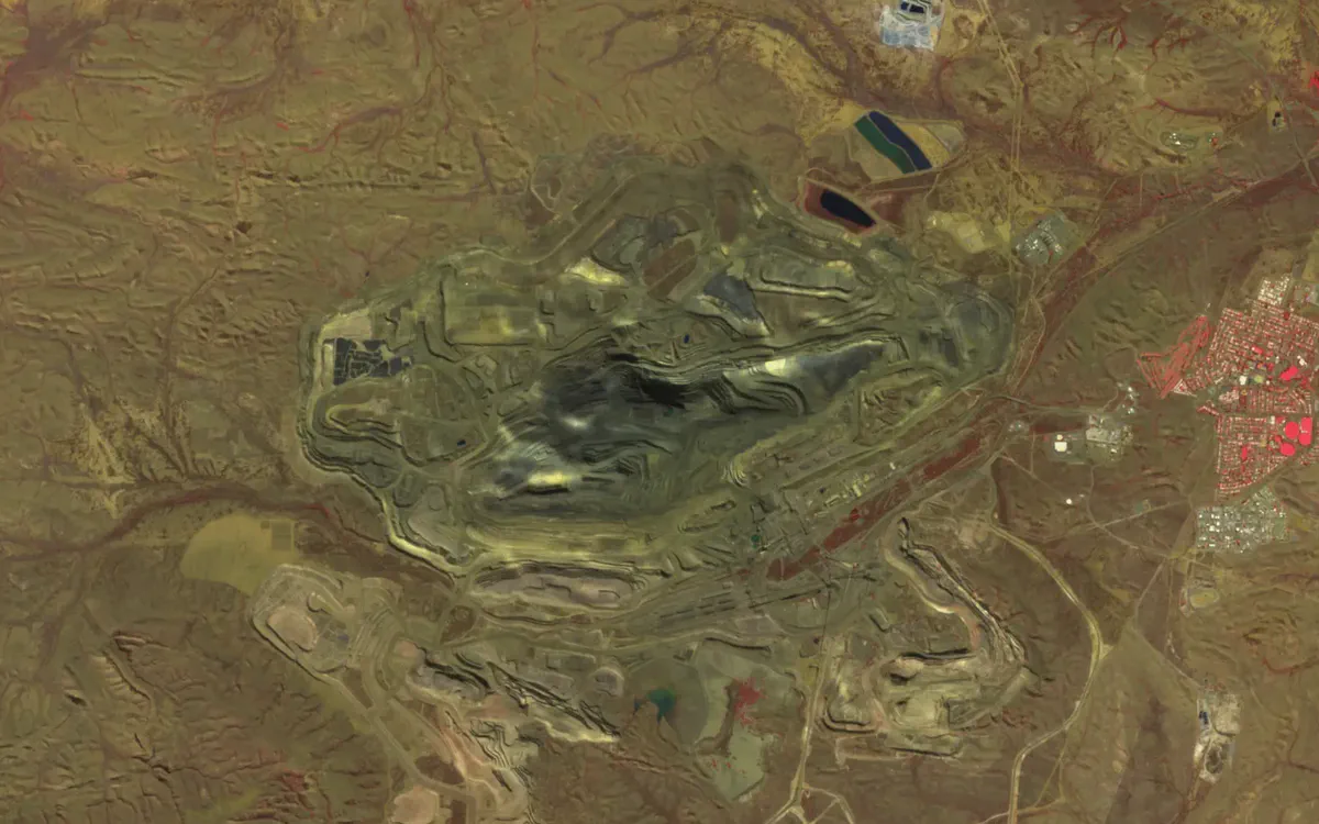 Mount Whaleback open-cut pit with terraced benches and waste dumps, and the town of Newman to the east